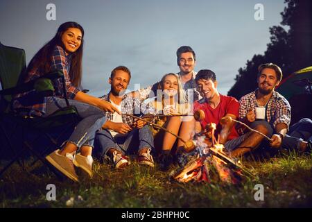 Lagerfeuer in der Nacht auf einem Hintergrund junger lächelnder Menschen bei einem Picknick im Herbst Stockfoto