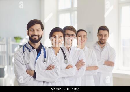 Eine Gruppe von selbstbewussten Praktizierenden Ärzten in weißen Mänteln lächelt vor dem Hintergrund der Klinik. Stockfoto