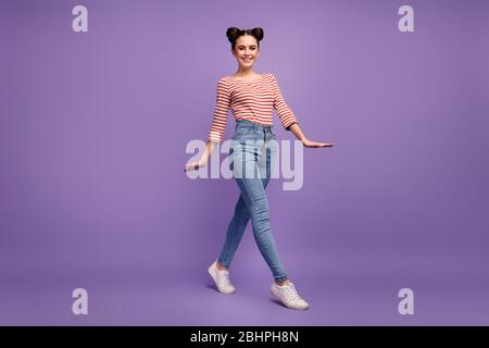 In voller Länge Profil Foto von hübschen Dame Teenager zwei Brötchen gute Laune Spaziergang Straße tragen weiß rot lässig gestreiftes Hemd Jeans Schuhe isoliert lila Stockfoto