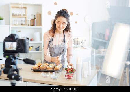 Professionelle Bäcker zu Hause stehend Küche Dekoration frische Cupcakes mit süßer Sahne, Aufnahmeprozess vor der Kamera Stockfoto