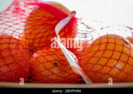 Orangen in Plastikgeflettstoff auf einer Platte. Stapeln Sie frische Orangen in Kunststoff roten Mesh-Sack Stockfoto