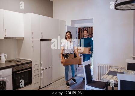 Ein attraktiver kaukasischer Mann und eine attraktive Frau betreten eine neue Wohnung mit Schachteln. Ein liebevolles Paar zieht ein Stockfoto
