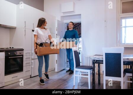 Ein attraktiver kaukasischer Mann und eine attraktive Frau betreten eine neue Wohnung mit Schachteln. Ein liebevolles Paar zieht ein Stockfoto