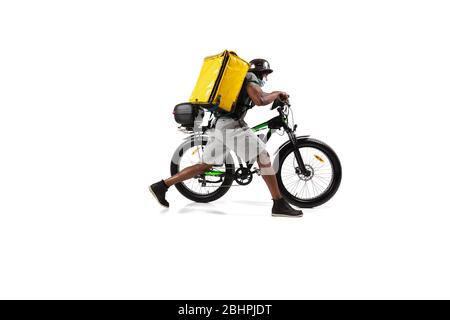 Zu viele Bestellungen. Kontaktloser Lieferservice während der Quarantäne. Der Mann liefert Nahrung während der Isolation, trägt Helm und Gesichtsmaske. Essen auf dem Fahrrad auf weißem Hintergrund isoliert. Sicherheit. Schnell nach oben. Stockfoto