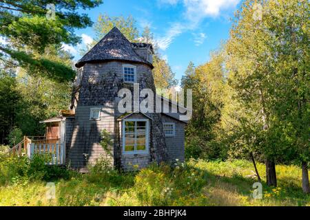 Ein verlassene Haus in einem Feld im Wald. Das Haus hat einen Turm, der nach einer holländischen Windmühle gestaltet ist. Die hölzernen Schindeln verrotten, und der Teil Stockfoto