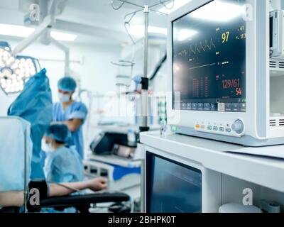 Die Überwachung der Vitalfunktionen des Patienten im Operationssaal ist im Fokus. Vor dem Hintergrund einer starken Unschärfe, Chirurgen Stockfoto