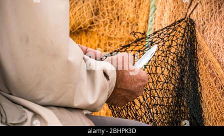 Nahaufnahme des Fischers, der das Fischernetz mit dem Messer repariert. Stockfoto