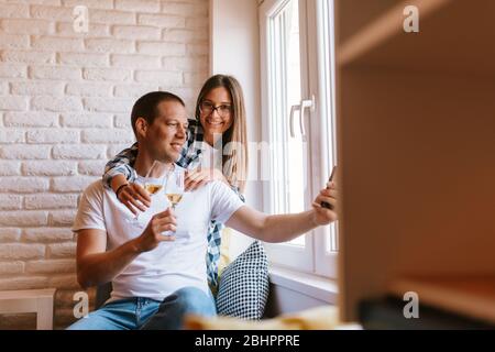 Schönes lächelndes kaukasisches Paar mit Gläsern Wein bei der Fenster in der Wohnung Stockfoto