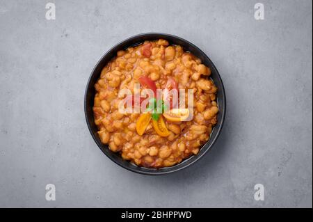 Ful Medanes oder Fava Bohnen in schwarzer Schale vor grauer Kulisse. Foul Mudammas ist ein ägyptisches, libanesisches, syrisches, eritreisches, israelisches Gericht Frühstück Stockfoto