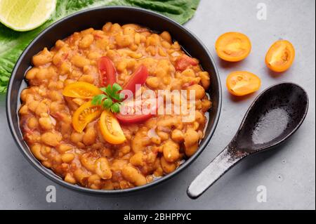 Ful Medanes oder Fava Bohnen in schwarzer Schale vor grauer Kulisse. Foul Mudammas ist ein ägyptisches, libanesisches, syrisches, eritreisches, israelisches Gericht Frühstück Stockfoto