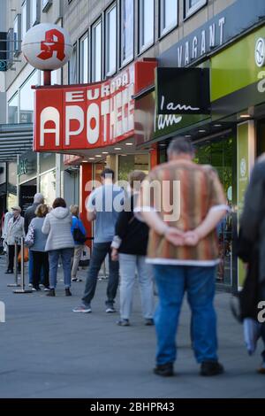 Hannover, Deutschland. April 2020. Passanten stehen vor einer Apotheke im Stadtzentrum Schlange. Seit Montag sind in Niedersachsen Masken für öffentliche Verkehrsmittel und Geschäfte Pflicht. Kredit: Ole Spata/dpa/Alamy Live News Stockfoto