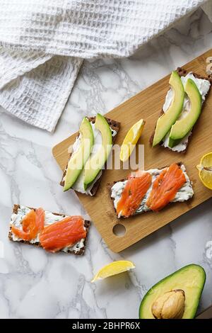 Frühstück am Morgen, zartes hausgemachtes Weichkäse auf Crackern mit geräucherter Forelle und Avocado Stockfoto