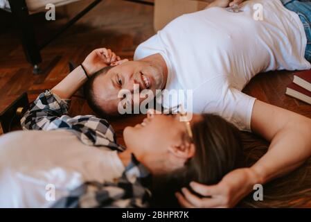 Ein Freund und eine Freundin feiern den Umzug in eine neue Wohnung. Liebes Paar, das auf dem Boden liegt und Wein trinkt Stockfoto