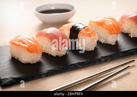 Eine Reihe von frischem Nighiri-Sushi, garniert mit rohen Lachsscheiben auf Reis und dekoriert mit Nori auf einem schwarzen Tablett in der Nähe einer Sushi-Bar oder Restaurant Stockfoto