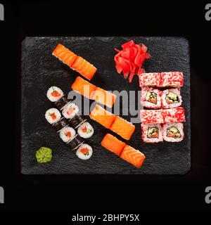 Japanisches Restaurant, Sushi-Rolle auf schwarzem Schiefer. Set für zwei Personen mit Ingwer und Wasabi auf dunklem Hintergrund. Stockfoto