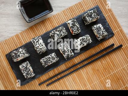 Minimalismus und Raffinesse: Köstlicher Lachs und Avocado-Sushi mit schwarzen Sesamkörnern. Serviert mit Ingwer und Wasabi auf einem schwarzen Stein. Stockfoto