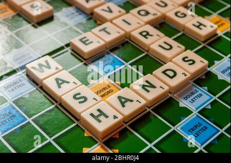 Worte auf einem Scrabble-Brett in Bezug auf die Coronavirus/Covid-19-Pandemie mit 'Wash Hands' im Fokus. Stockfoto