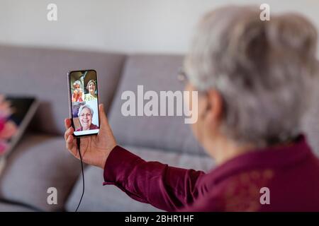 Eine Frau, die ein Mobiltelefon hält und während der sozialen Isolation, skype oder whatsapp Party drei Freunde auf dem Bildschirm ansieht. Stockfoto