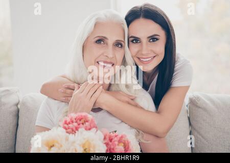 Nahaufnahme Foto von zwei Menschen weiß grau Haar pensionierte Oma halten große Blüte Blüte Pfingstrose sie erhalten 8-märz Veranstaltung Tochter Umarmung kuscheln Couch sitzen Stockfoto