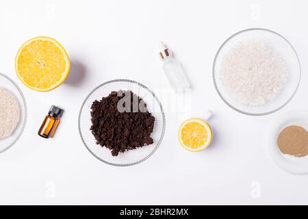 Natürliche Schönheitsprodukte für die Herstellung von hausgemachten Körperpeeling aus gemahlenem Kaffee, Ton, Meersalz und Zitrusfrüchten ätherischen Ölen, flach auf weißem Hintergrund. Stockfoto