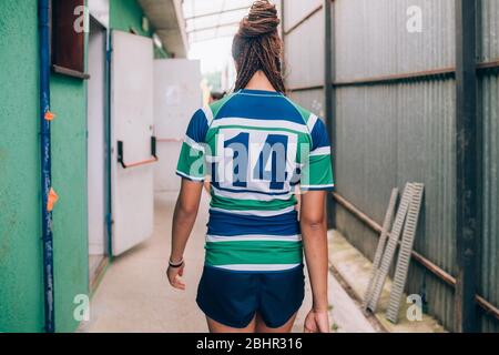 Rückansicht einer Frau, die ein grünes, blau-weißes Rugby-Shirt trägt und zu den Umkleidekabinen geht. Stockfoto