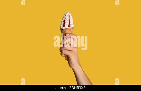 Millennial Kerl mit leckeren Eis mit Obst Topping in Waffel-Kegel, orange Hintergrund, Nahaufnahme. Panorama Stockfoto