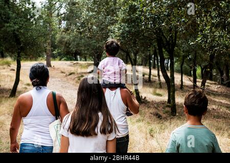 Rückansicht der Familie mit drei Kindern, die auf dem Weg durch einen Wald spazieren. Stockfoto