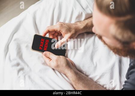 Fake News Infosemics during Covid-19 Pandemie Concept. Mann hält Handy und liest zu Hause Nachrichten oder soziale Netzwerke. Letzte News lesen upd Stockfoto