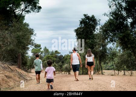 Rückansicht der Familie mit zwei Kindern, die auf einem Feldweg durch einen Wald laufen. Stockfoto