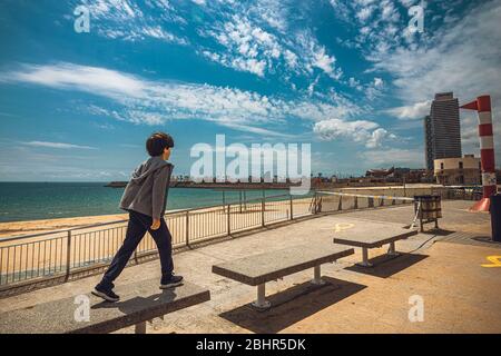 Barcelona, Spanien. April 2020. Ein Junge springt am verlassenen und abgesperrten Strand in Barcelona über Bänke am Tag, nachdem Spanien die Sperrstunde für unter 14 Jahre erleichtert hat und ihnen nach sechs Wochen einer landesweiten Sperrung aufgrund der kontinuierlichen Ausbreitung einen einstündigen begleiteten Spaziergang durch die nahe Nachbarschaft gewährt Des Corona-Virus. Spanien verzeichnete bis jetzt rund 300 neue Todesfälle mit einer Todesrate von fast 23500 Todesfällen. Quelle: Matthias Oesterle/Alamy Live News Stockfoto