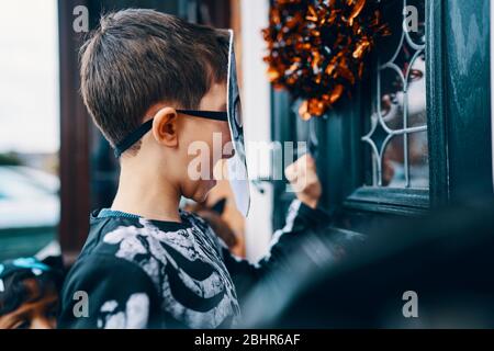 Nahaufnahme eines Jungen, der an Halloween eine Maske trägt und an eine Haustür klopft. Stockfoto