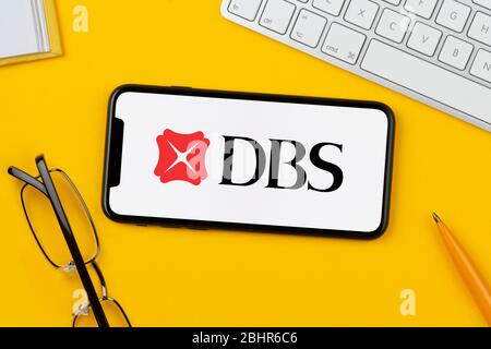 Ein Smartphone mit dem Logo der DBS Bank liegt auf einem gelben Hintergrund zusammen mit Tastatur, Brille, Stift und Buch (nur für redaktionelle Verwendung). Stockfoto