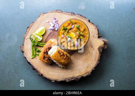 Berühmte indische Street Food pav bhaji auf einem Holzteller auf grauem Hintergrund dekoriert und mit rohen Zwiebel Zitrone und grünen Chilis garniert Stockfoto