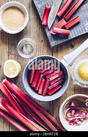 Schüssel mit Stücken von frisch gepflückten Stielen von Bio-Rhabarber auf einem Holzhintergrund mit Zutaten. Schritt für Schritt Rezept von pochierten Rhabarber. Serie. Bis Stockfoto