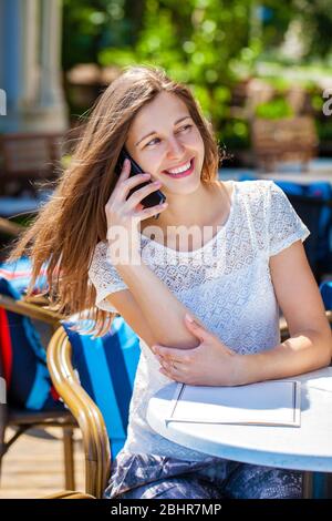 Glücklich Brünette Frau anrufen per Telefon im Open-Air-café Stockfoto