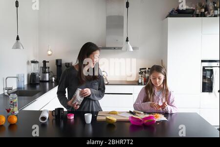 Home Life, ein Schulmorgen während der Lockdown. Ein Mädchen und ihre Mutter kochen zusammen in einer Küche Stockfoto