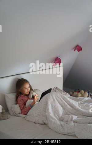 Home Life, ein Schulmorgen während der Lockdown. Ein Mädchen, das mit einem digitalen Tablet im Bett liegt. Stockfoto