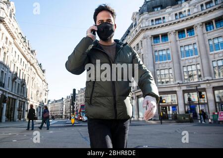 Ein Mann, der eine Gesichtsmaske und Plastikhandschuhe trägt, geht die Oxford Street entlang und spricht mit einem Handy. Stockfoto