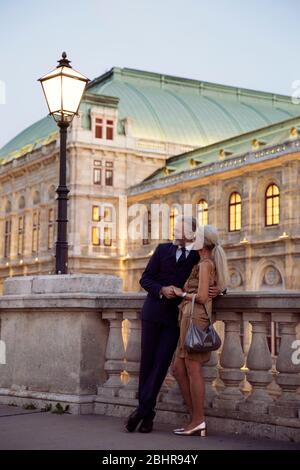 Ein Paar, das Arm in Arm gegen eine Balustrade lehnt, während des frühen Abends in Wien. Stockfoto
