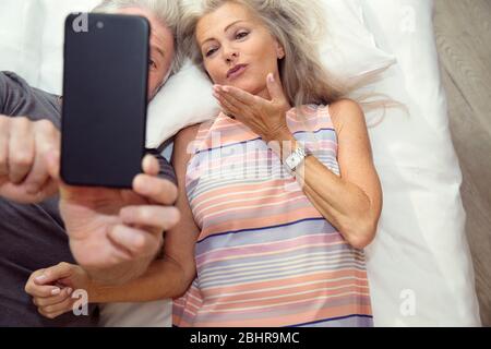 Ein Paar, das auf einem Bett liegt und ein Selfie auf einem Handy nimmt. Stockfoto