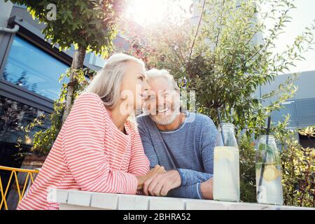 Ein Paar sitzt an einem Tisch im Garten mit Getränken in Flaschen. Stockfoto