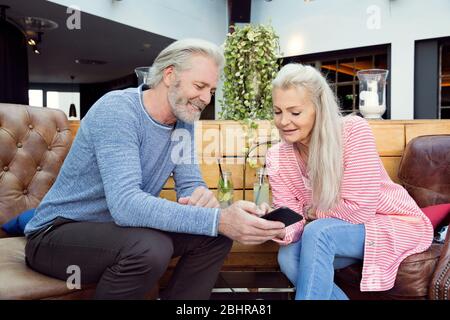Ein Paar sitzt an der Hotelrezeption und schaut sich zusammen ein Mobiltelefon an. Stockfoto