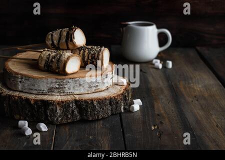 Gebratene Marshmallows auf einem Stock in Schokolade Glasur und gekrönt mit graham Cracker. Alternative Biskuit-smor. Dunkler rustikaler Stil. Stockfoto