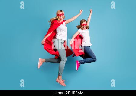 Ganzkörper-Foto von lustigen Mutter Dame kleine Tochter verbringen Zeit zusammen Karneval super Held Kostüme springen hoch bis Heben Fäuste tragen s-Shirts roten Mantel Stockfoto