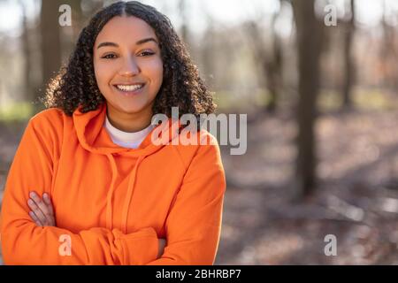 Outdoor-Porträt von schönen glücklich gemischten Rasse biracial afro-amerikanischen Mädchen Teenager weiblich junge Frau Arme gefaltet Lachen und lächeln mit Ma Stockfoto