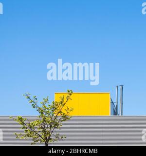 Minimalistische Industriearchitektur gegen blauen Himmel mit grünen Baumdetails, minimalistisches Konzept mit farbenfrohem Industriegebäude Stockfoto