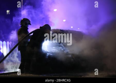 Feuerwehrleute kämpfen gegen das Feuer in der Mitternacht. Polizeiauto in einem Rücken. Stockfoto