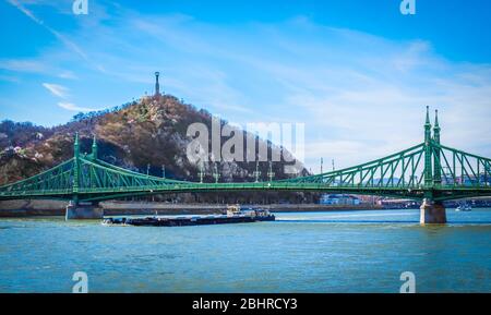 Budapest, Ungarn, März 2020 Blick auf einen Lastkahn, der unter der Freiheitsbrücke über die Donau verläuft Stockfoto