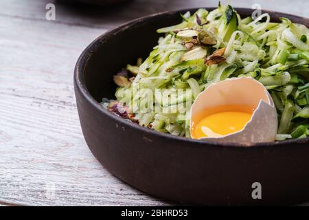 Zutaten für Zucchini-Fritten, vegetarische Gerichte mit frisch geriebenen Zucchini, Eigelb, Pistazien und Gewürze in rustikaler Keramikschale, so Stockfoto
