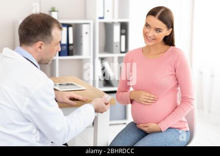 Ältere erfahrene Arzt zeigt Pillen für schwangere Patienten Stockfoto